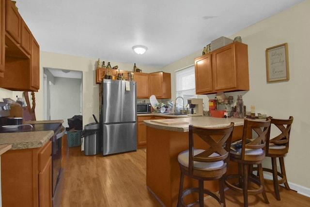 kitchen with a breakfast bar, sink, kitchen peninsula, stainless steel appliances, and light hardwood / wood-style floors