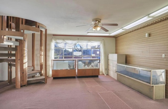 misc room featuring carpet flooring, crown molding, ceiling fan, and wood walls