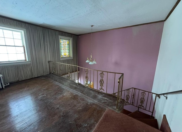 stairway with crown molding, wood-type flooring, a textured ceiling, and a notable chandelier