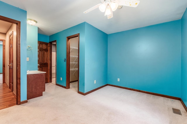 unfurnished bedroom with ceiling fan, light colored carpet, a spacious closet, and a closet