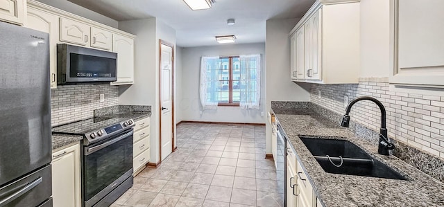 kitchen with white cabinetry, sink, stainless steel appliances, and dark stone counters