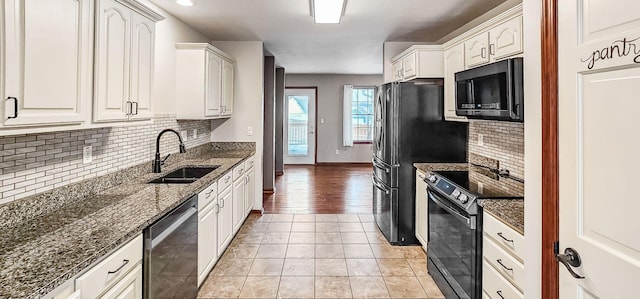 kitchen with stainless steel appliances, white cabinetry, sink, and dark stone counters