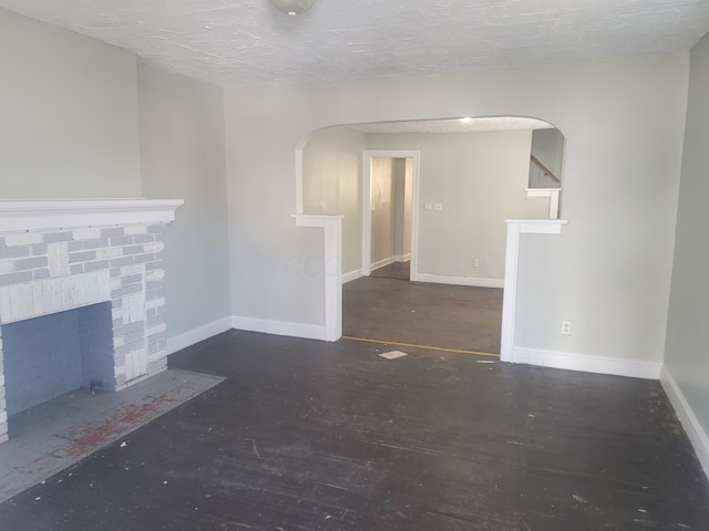 unfurnished living room with dark wood-type flooring, a brick fireplace, and a textured ceiling