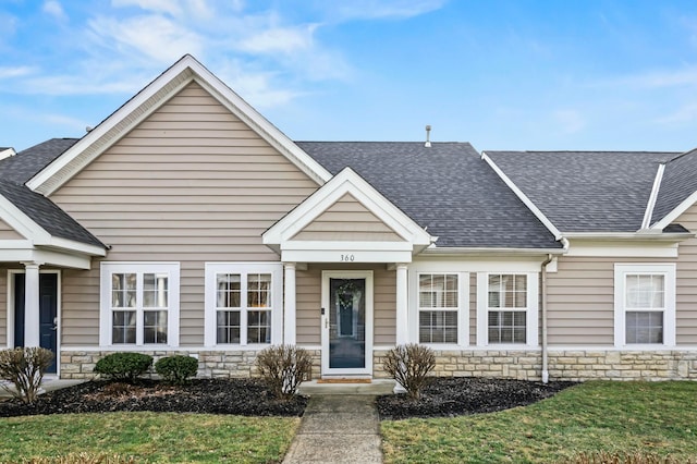 view of front of home featuring a shingled roof, stone siding, and a front lawn