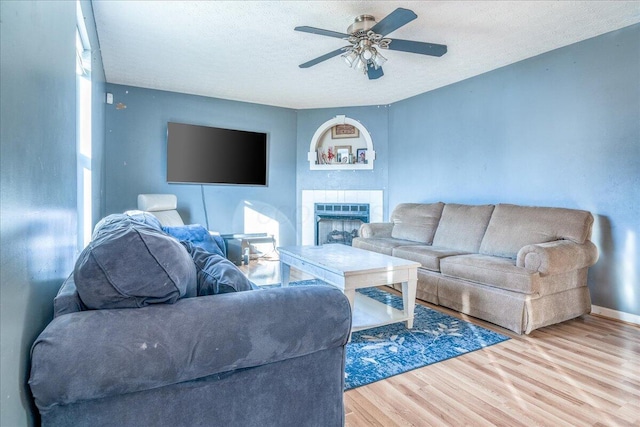 living room with hardwood / wood-style flooring, ceiling fan, a fireplace, and a textured ceiling