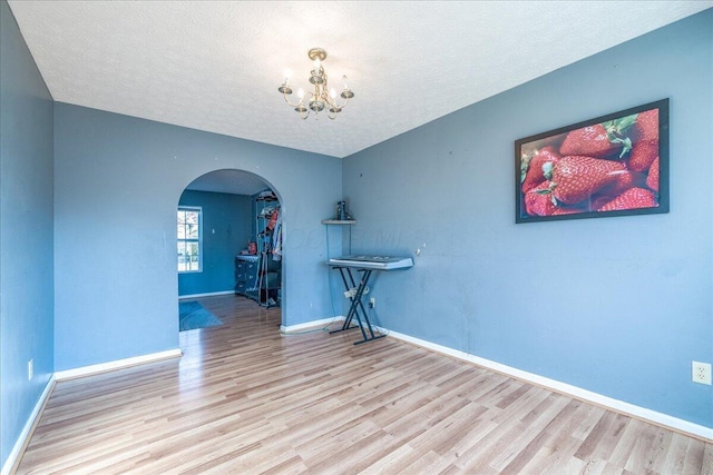 spare room with an inviting chandelier, light hardwood / wood-style flooring, and a textured ceiling