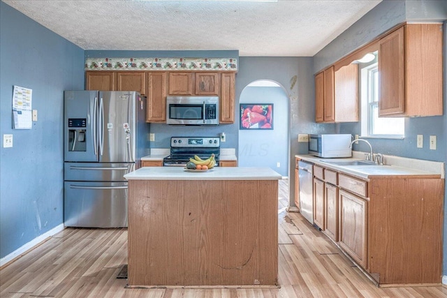 kitchen featuring stainless steel appliances, a kitchen island, light wood-type flooring, and a textured ceiling