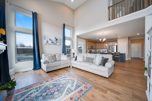 living room featuring an inviting chandelier, a towering ceiling, and light wood-type flooring