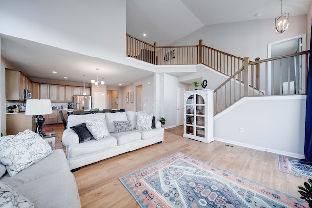 living room with high vaulted ceiling, a chandelier, and light hardwood / wood-style floors