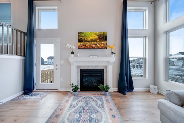 living room featuring a healthy amount of sunlight, a tiled fireplace, light hardwood / wood-style floors, and a high ceiling