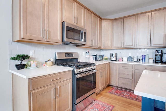 kitchen with appliances with stainless steel finishes, light brown cabinets, backsplash, and light hardwood / wood-style floors