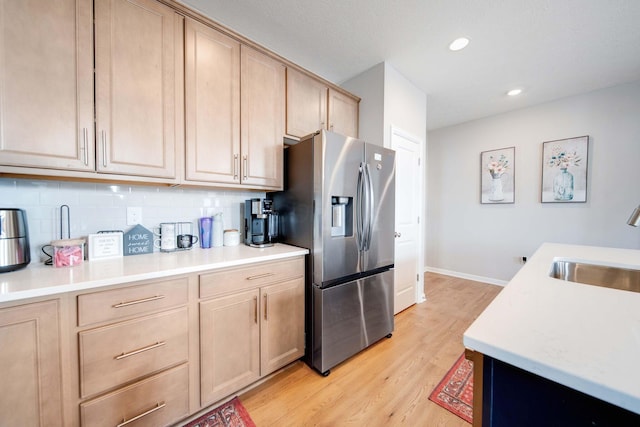 kitchen with sink, backsplash, stainless steel fridge with ice dispenser, light brown cabinets, and light hardwood / wood-style flooring