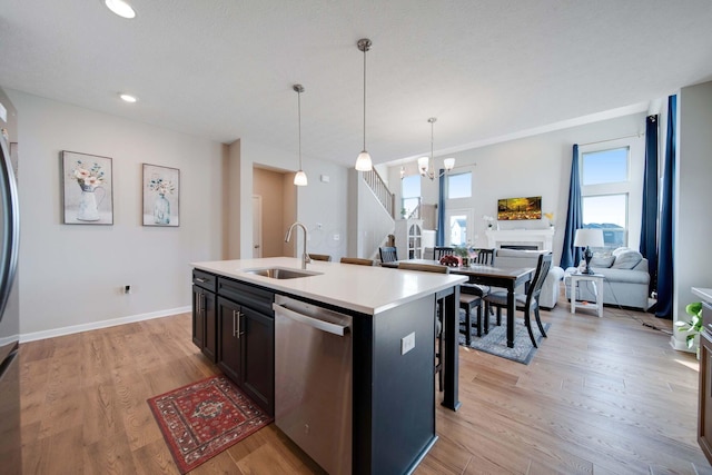 kitchen with sink, decorative light fixtures, light wood-type flooring, stainless steel dishwasher, and an island with sink