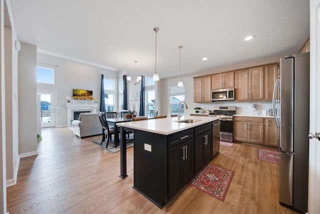 kitchen with pendant lighting, sink, light hardwood / wood-style floors, stainless steel appliances, and a center island with sink