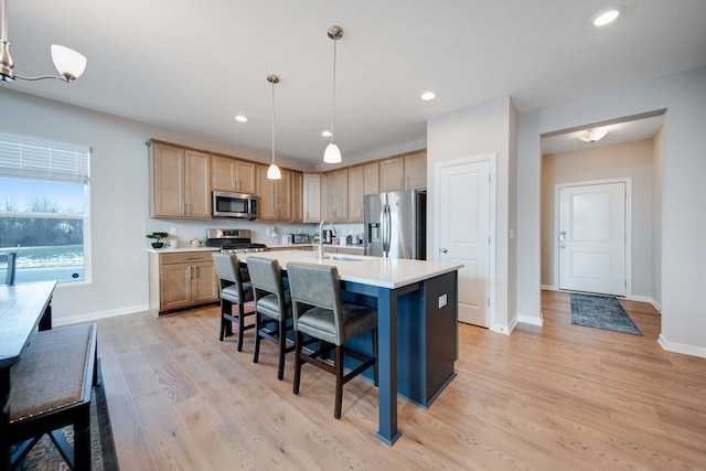 kitchen featuring pendant lighting, light hardwood / wood-style flooring, appliances with stainless steel finishes, a kitchen breakfast bar, and a center island with sink