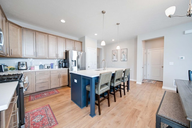 kitchen featuring pendant lighting, appliances with stainless steel finishes, tasteful backsplash, a center island with sink, and light wood-type flooring