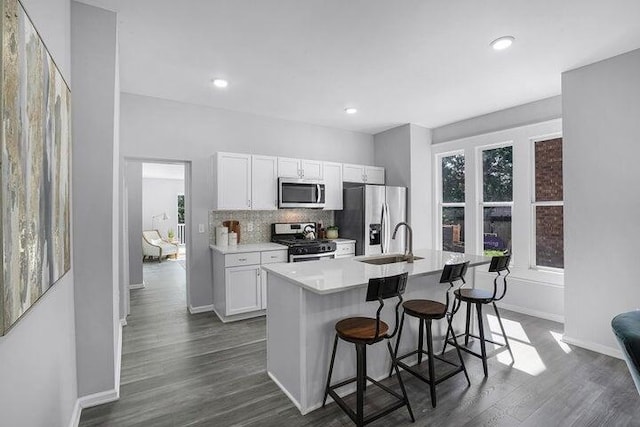 kitchen with tasteful backsplash, white cabinetry, an island with sink, a kitchen breakfast bar, and stainless steel appliances