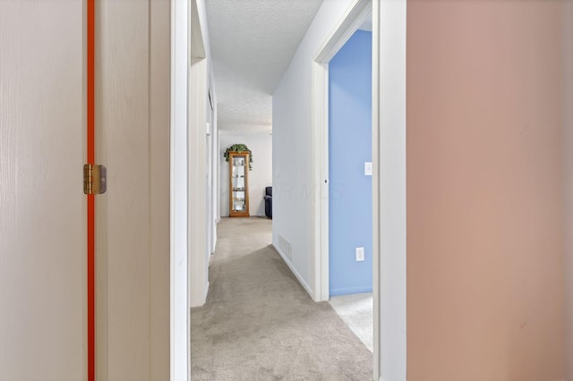 hall with light carpet and a textured ceiling