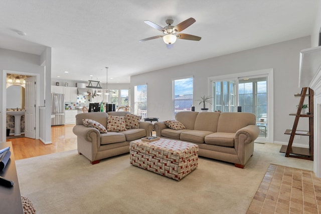 living room featuring light colored carpet, sink, and ceiling fan with notable chandelier