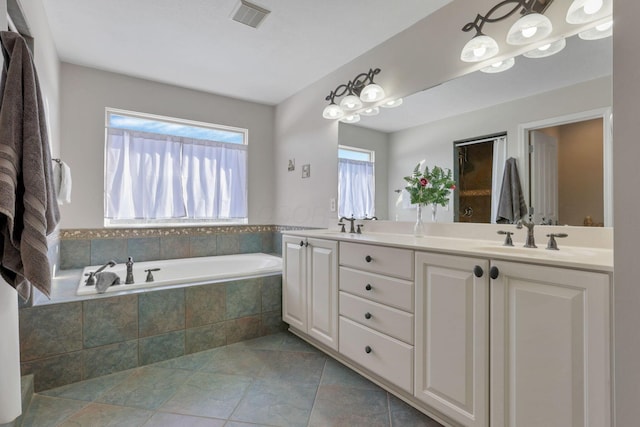 bathroom featuring a healthy amount of sunlight, vanity, and tiled bath