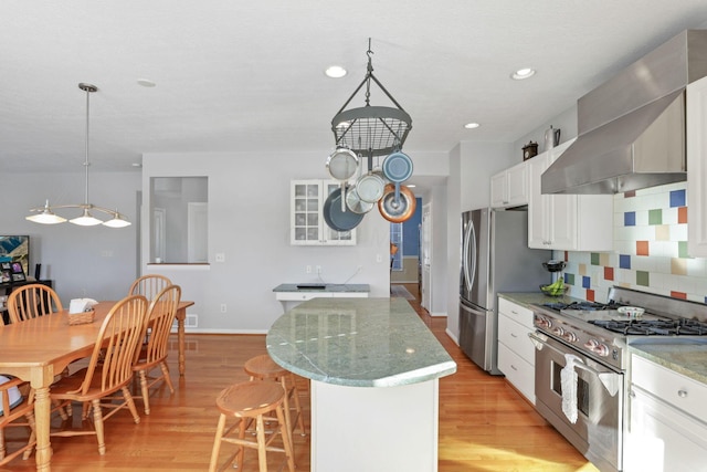 kitchen with a kitchen island, white cabinets, stainless steel appliances, wall chimney range hood, and light hardwood / wood-style flooring