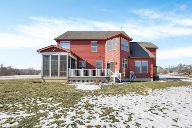 snow covered back of property featuring a deck, a sunroom, and a lawn