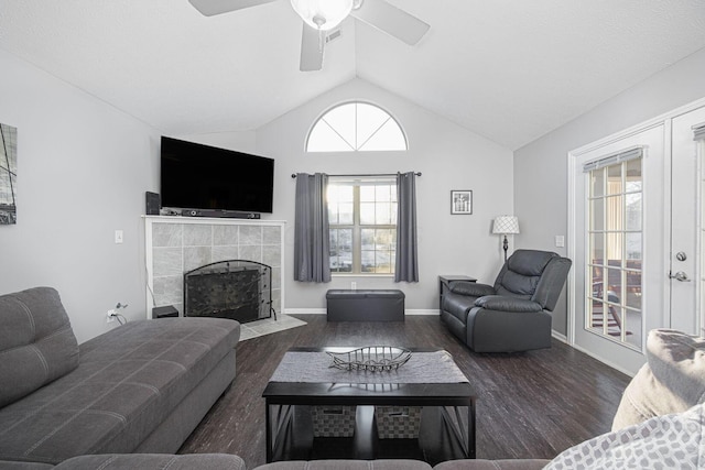 living room with dark wood-type flooring, french doors, lofted ceiling, ceiling fan, and a tiled fireplace