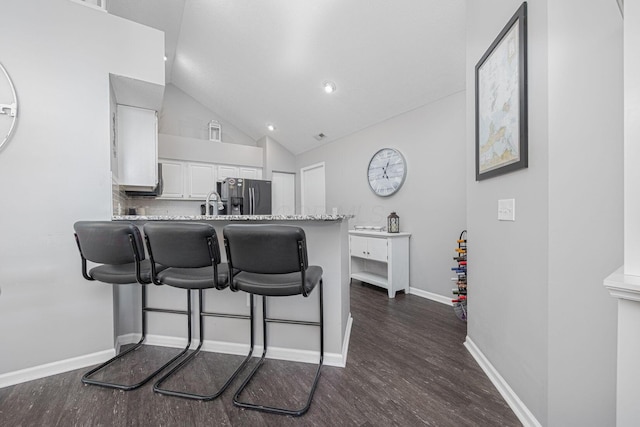 kitchen featuring white cabinetry, stainless steel fridge, dark hardwood / wood-style flooring, a kitchen bar, and kitchen peninsula