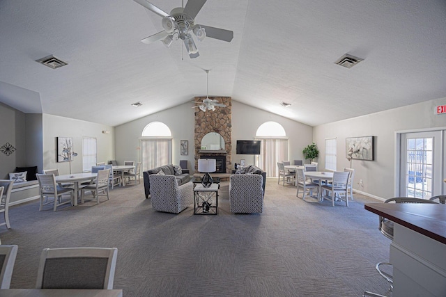 carpeted living room with ceiling fan, a stone fireplace, vaulted ceiling, and a textured ceiling