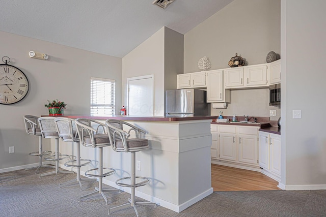 kitchen featuring white cabinetry, appliances with stainless steel finishes, a breakfast bar, and light carpet