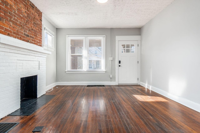 foyer entrance featuring a brick fireplace, dark wood-type flooring, and a textured ceiling