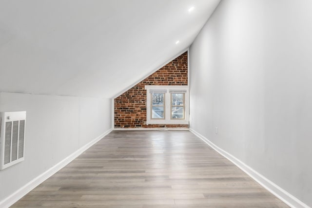 additional living space with hardwood / wood-style flooring, vaulted ceiling, and brick wall