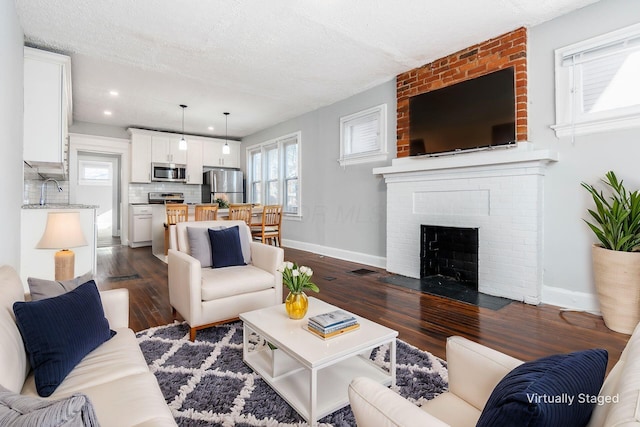 living room featuring a brick fireplace, dark wood-type flooring, sink, and a textured ceiling