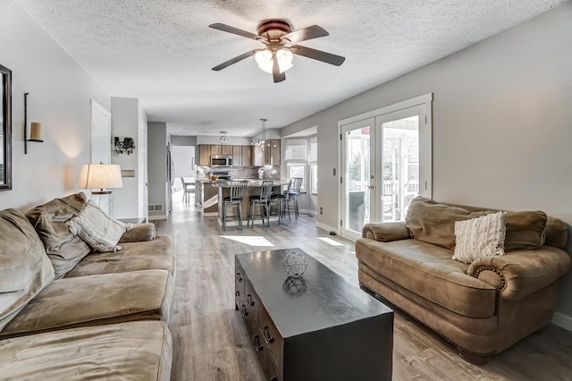 living room with ceiling fan, a textured ceiling, light wood-type flooring, and french doors