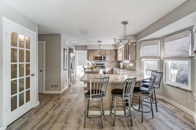 kitchen with pendant lighting, sink, backsplash, stainless steel appliances, and kitchen peninsula