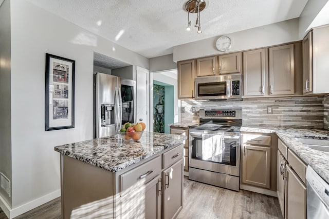 kitchen featuring appliances with stainless steel finishes, backsplash, a center island, light stone countertops, and light wood-type flooring