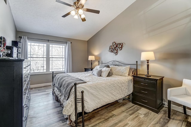 bedroom with ceiling fan, lofted ceiling, light hardwood / wood-style floors, and a textured ceiling