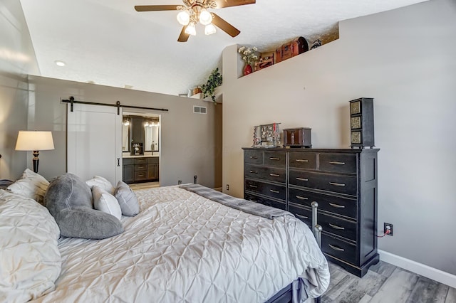 bedroom featuring lofted ceiling, ensuite bathroom, ceiling fan, a barn door, and light hardwood / wood-style floors