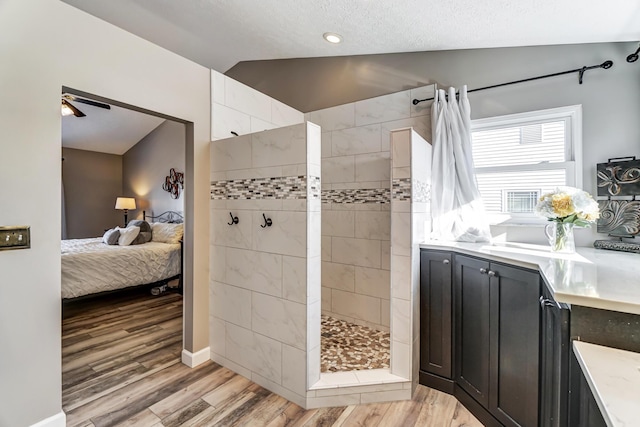 bathroom with vanity, wood-type flooring, tiled shower, and vaulted ceiling