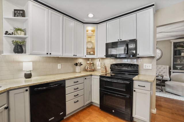 kitchen featuring light stone counters, white cabinets, light wood-type flooring, and black appliances