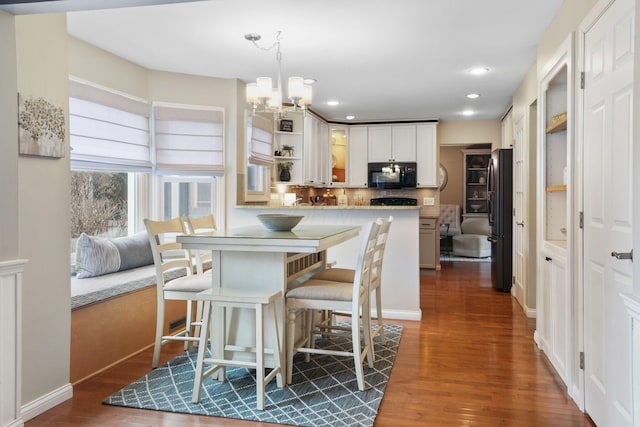 kitchen featuring an inviting chandelier, black appliances, hanging light fixtures, dark hardwood / wood-style flooring, and white cabinets