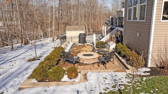 snowy yard with a storage shed, a patio, and an outdoor fire pit