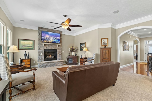 carpeted living room featuring crown molding, ceiling fan, and a stone fireplace