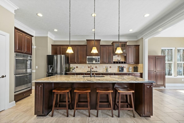 kitchen with appliances with stainless steel finishes, a kitchen breakfast bar, hanging light fixtures, light stone countertops, and a center island with sink