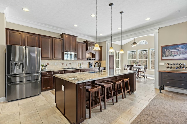 kitchen with pendant lighting, sink, a kitchen island with sink, stainless steel appliances, and light stone counters