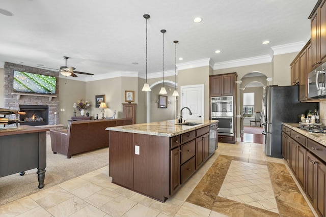 kitchen with pendant lighting, sink, appliances with stainless steel finishes, light stone counters, and a center island with sink