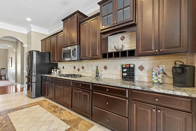 kitchen featuring crown molding, tasteful backsplash, dark brown cabinets, appliances with stainless steel finishes, and light stone countertops