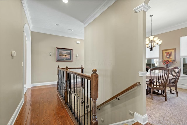 hallway with ornate columns, ornamental molding, hardwood / wood-style floors, and an inviting chandelier