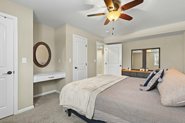 bedroom featuring light carpet, a textured ceiling, built in desk, and ceiling fan