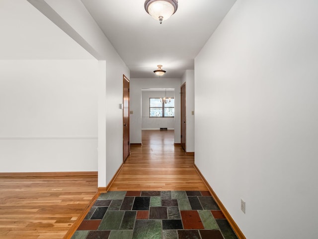 corridor featuring an inviting chandelier and hardwood / wood-style flooring